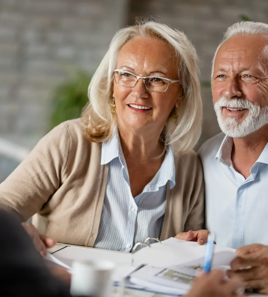 Happy mature couple talking to their real estate agent while going through paperwork on a meeting in the office.