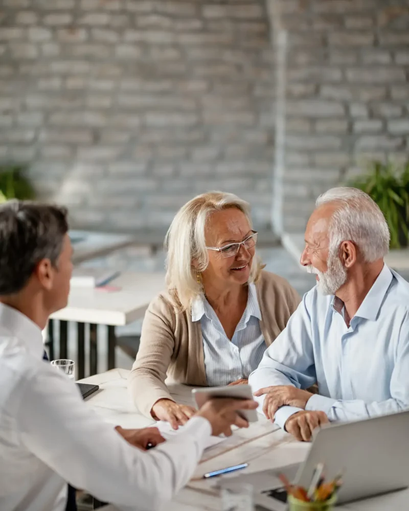 Happy senior woman talking to her husband while having a meeting with bank manager in the office.