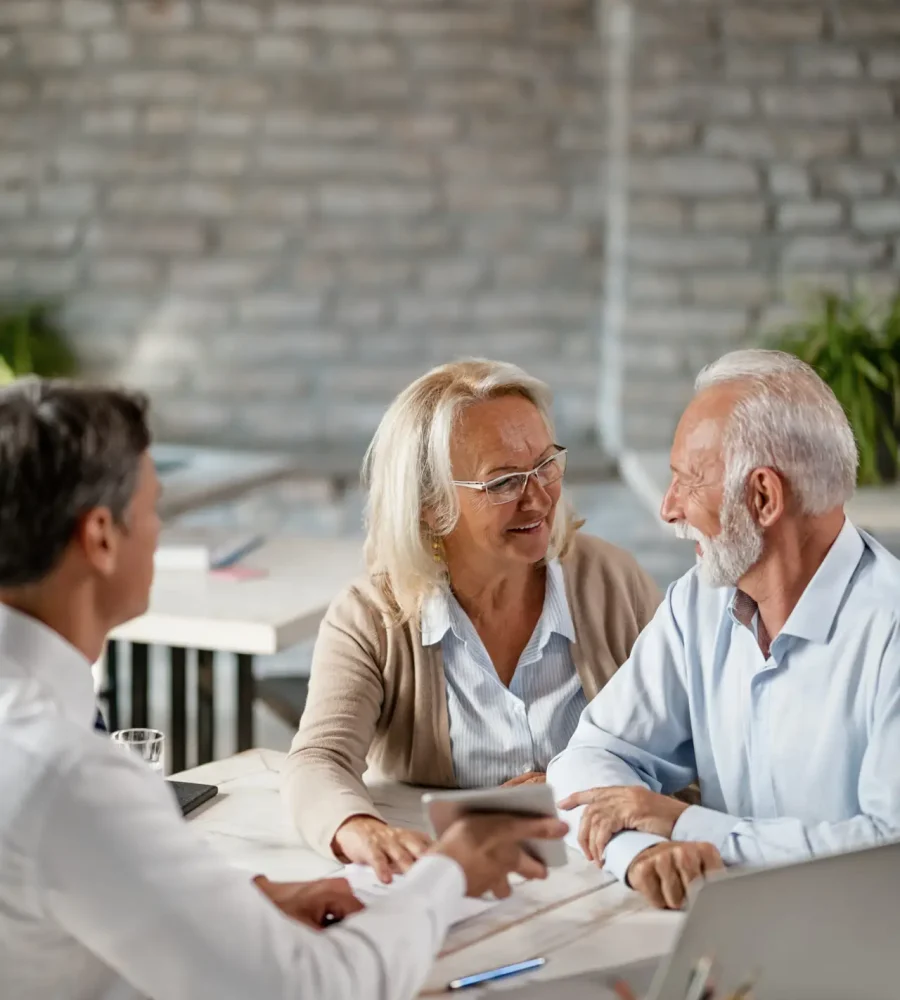 Happy senior woman talking to her husband while having a meeting with bank manager in the office.