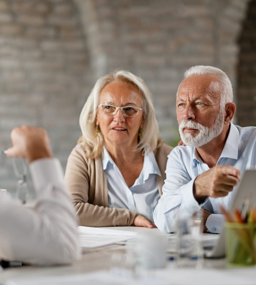 Senior man and his wife communicating with insurance agent while using computer during the consultations in the office. Senior man is pointing at something on a computer.